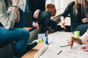 people gathered around a table with markers, pens, pencils and paper having a conversation and making notes on large pieces of paper for display